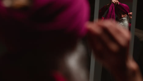 Low-Key-Studio-Lighting-Shot-Of-Senior-Sikh-Man-With-Beard-Tying-Fabric-For-Turban-Against-Dark-Background-Looking-In-Mirror-2